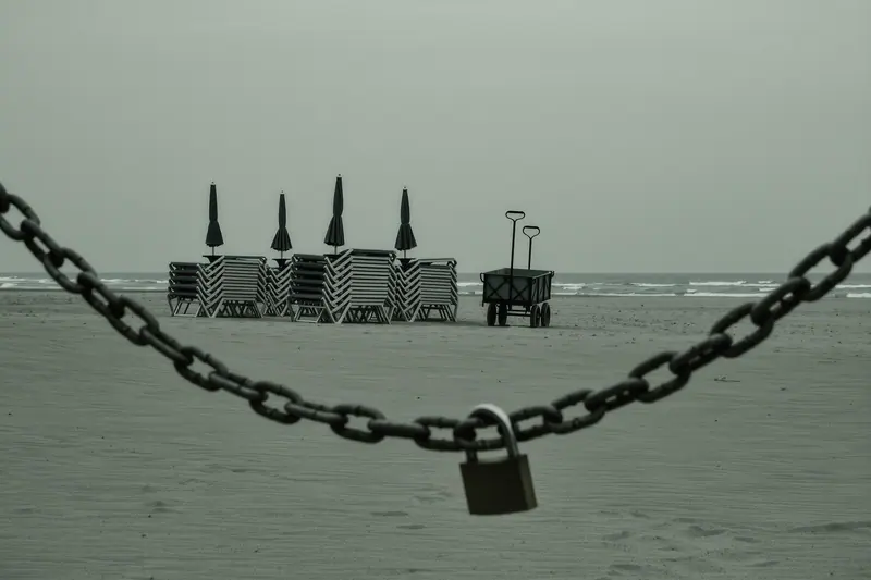 Stacked sun loungers, folded parasols and a beach cart chained together on the sand at the end of the day.
