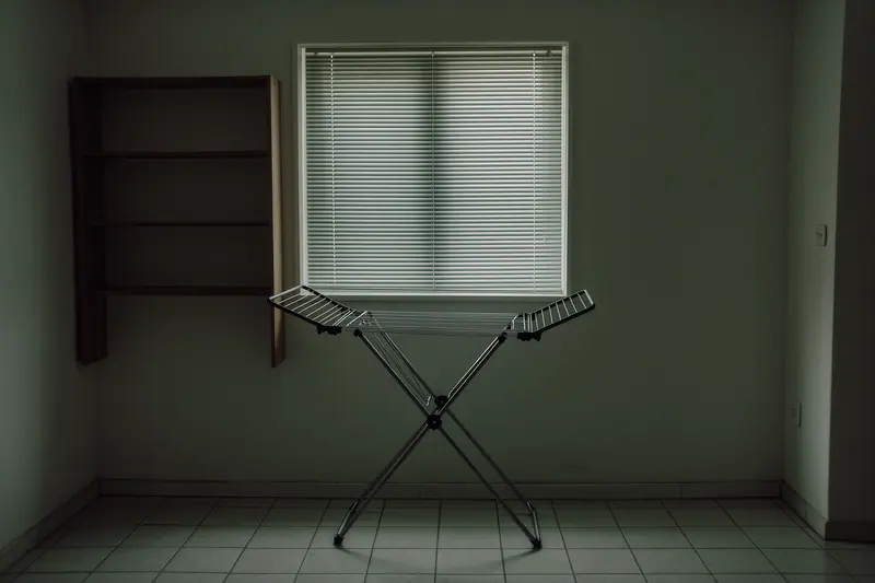 A plain long-let flat interior with a clothes drying rack, a shuttered window and empty shelves.