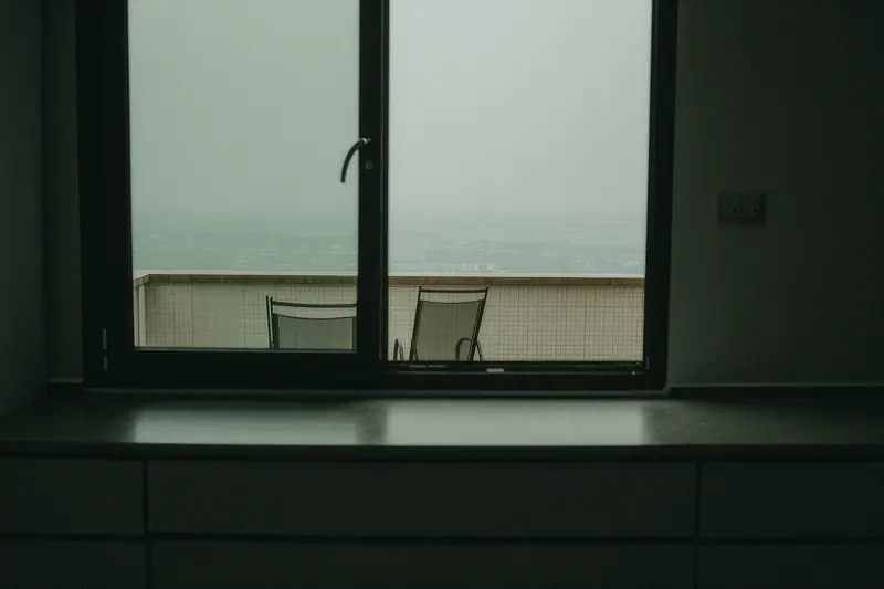 An empty holiday apartment with a tiled balcony, folded sun chairs and a bare kitchen counter.