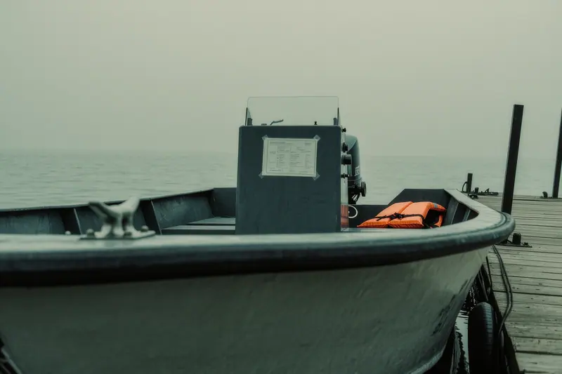 A small open boat tied at a pontoon, a laminated instruction card taped to the console and an orange life jacket lying on the seat.