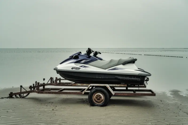 Two small jet skis on a launch trolley at the water's edge with a buoyed training area visible beyond them.
