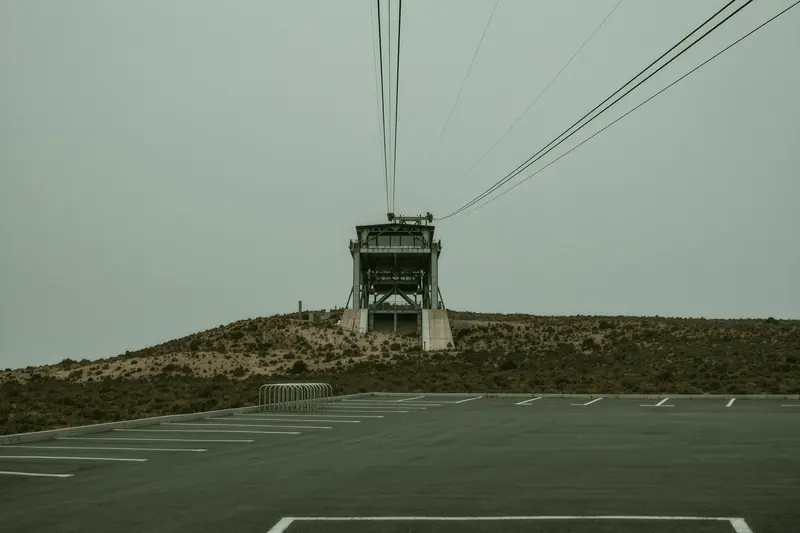 The lower station of a cable car on a dry hillside above the coast, with an empty car park and a bike rack.